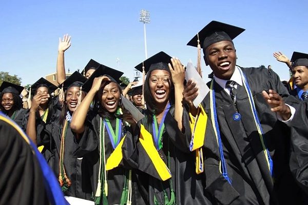 Diverse group of happy graduates in gowns cheering at graduation ceremony.